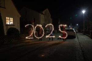 Sparkler light painting forming '2025' in a festive night street scene.